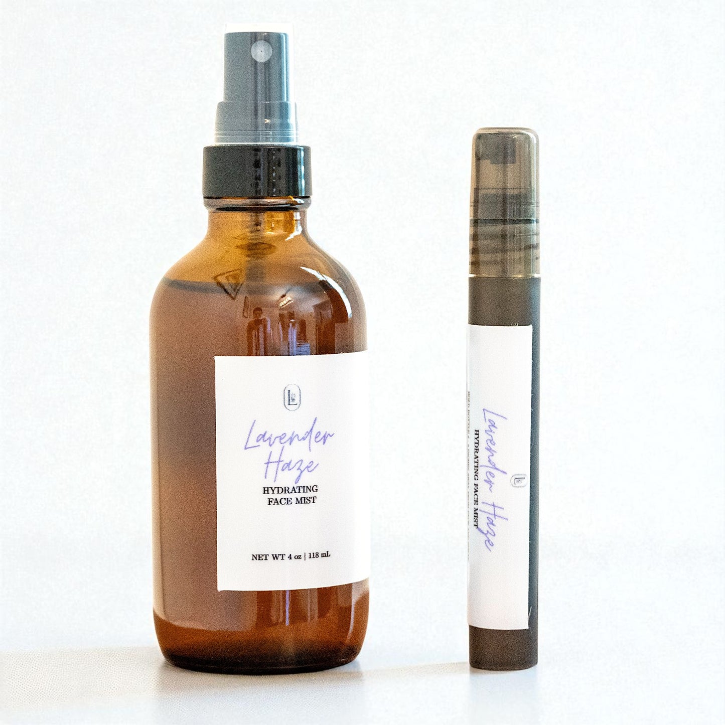 Brown glass bottle and black tube with white label of Lavender Haze Hydrating Face Mist on a light background