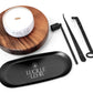 Lucille Lehr Candle Care Set with 'Melody XoXo' Candle: This complete set includes a stylish black tray, wick trimmer, snuffer, and wick dipper, designed to extend the life of your candle and ensure a clean burn. Paired with the 'Melody XoXo' candle on a wooden stand, this set brings elegance and functionality to your candle care routine.