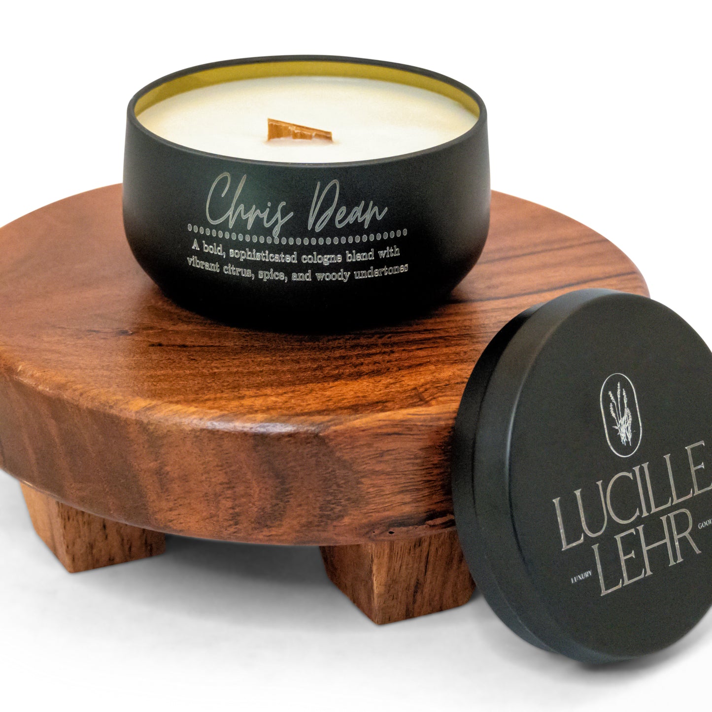 Lucille Lehr's 'Chris Dean' Candle: Embrace the bold sophistication of the 'Chris Dean' candle, blending vibrant citrus, spice, and woody undertones for a cologne-inspired scent. Presented in a sleek matte black tin with a crackling wooden wick, this candle sits on a rustic wooden stand, adding a refined and inviting aroma to any room.