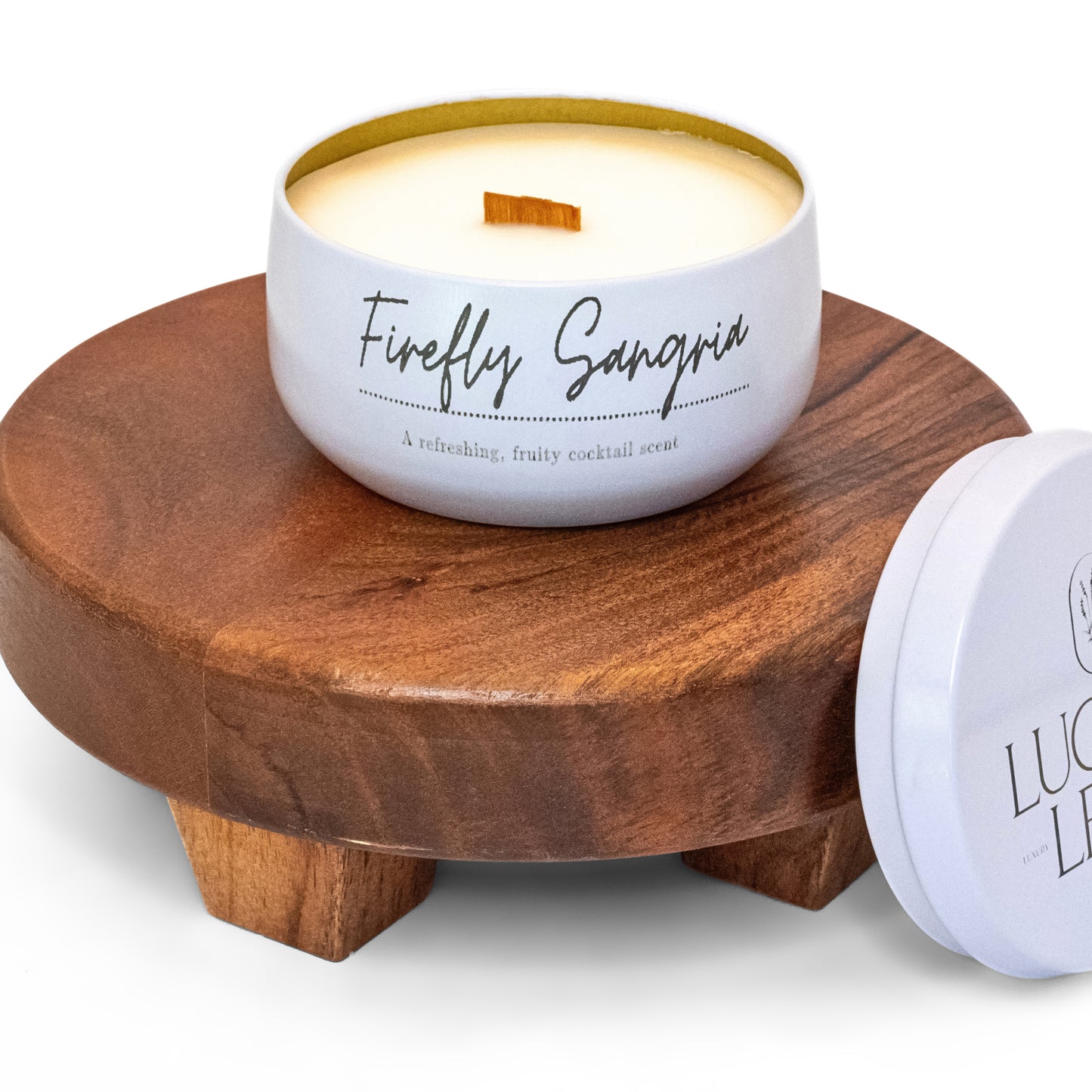 Lucille Lehr's 'Firefly Sangria' Candle: Infuse your space with the fruity, cocktail-inspired aroma of the 'Firefly Sangria' candle, featuring a refreshing blend that evokes the essence of a lively sangria. Presented in a white tin with a crackling wooden wick, this candle sits on a rustic wooden stand, adding a playful and invigorating ambiance to any setting.