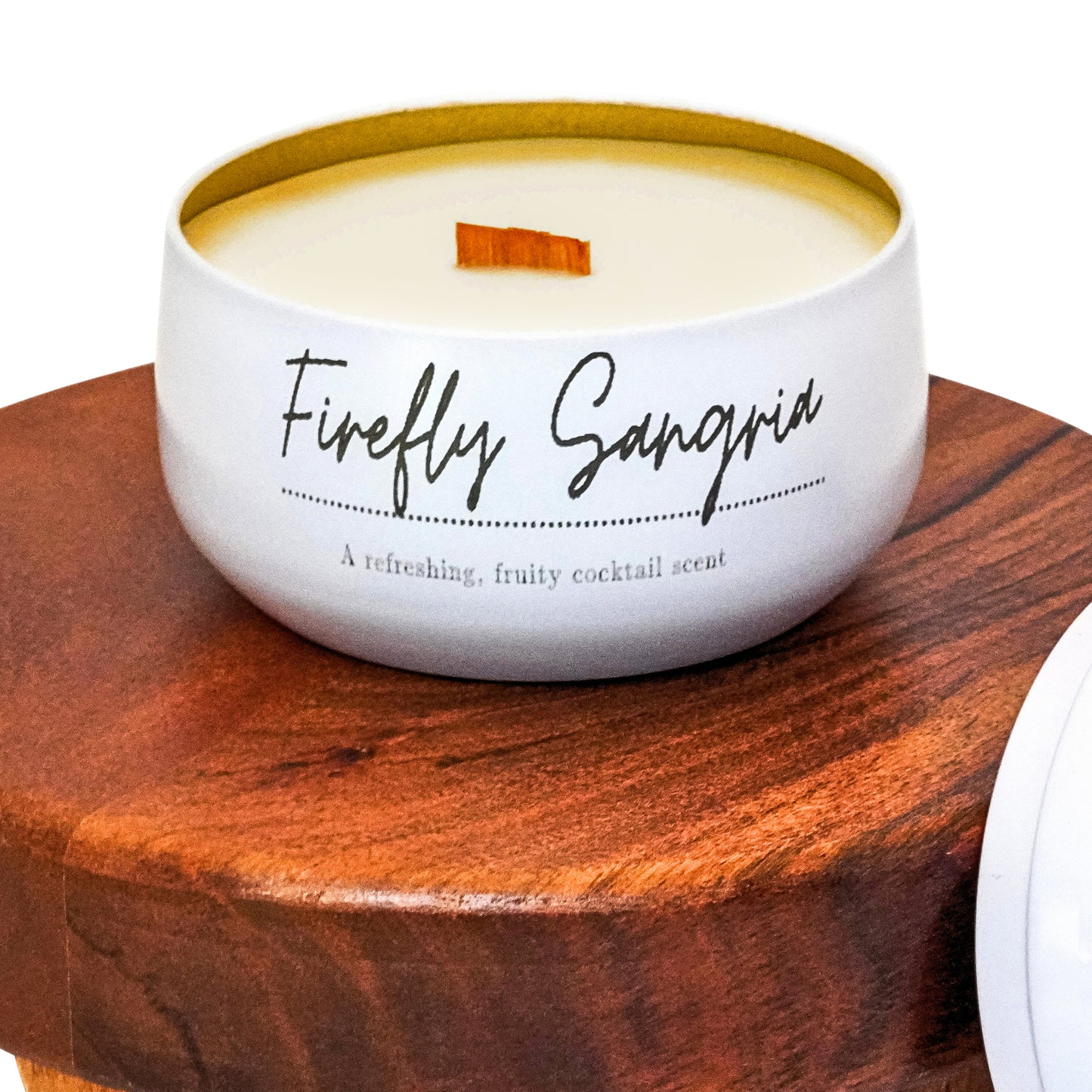 Up-close view of Lucille Lehr's 'Firefly Sangria' Candle: This refreshing candle captures the fruity, cocktail-inspired scent of sangria, perfect for brightening your space. Encased in a sleek white tin with a crackling wooden wick, the 'Firefly Sangria' candle brings a playful and invigorating aroma to any room.