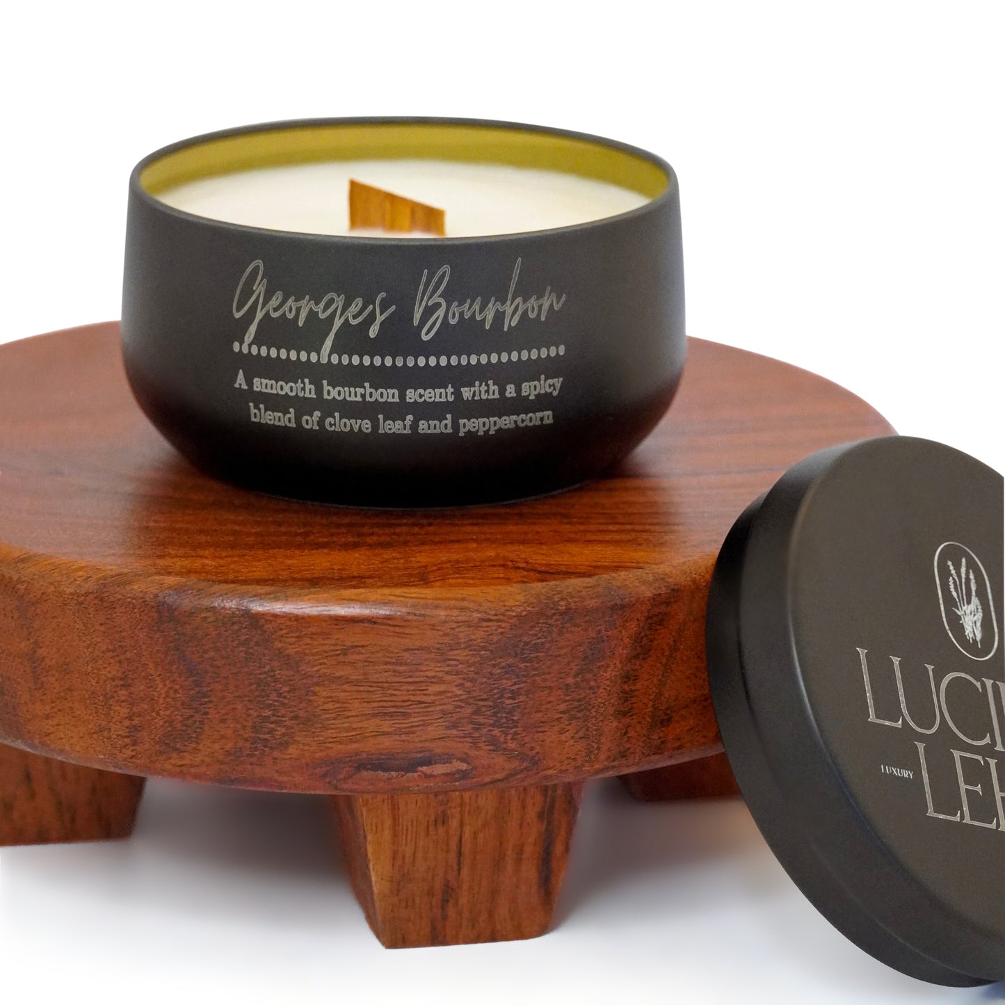 Lucille Lehr's 'Georges Bourbon' Candle: Immerse yourself in the refined aroma of the 'Georges Bourbon' candle, blending a smooth bourbon scent with spicy notes of clove leaf and peppercorn. Housed in a matte black tin with a wooden wick, this candle sits elegantly on a wooden stand, adding a cozy and sophisticated ambiance to any room.