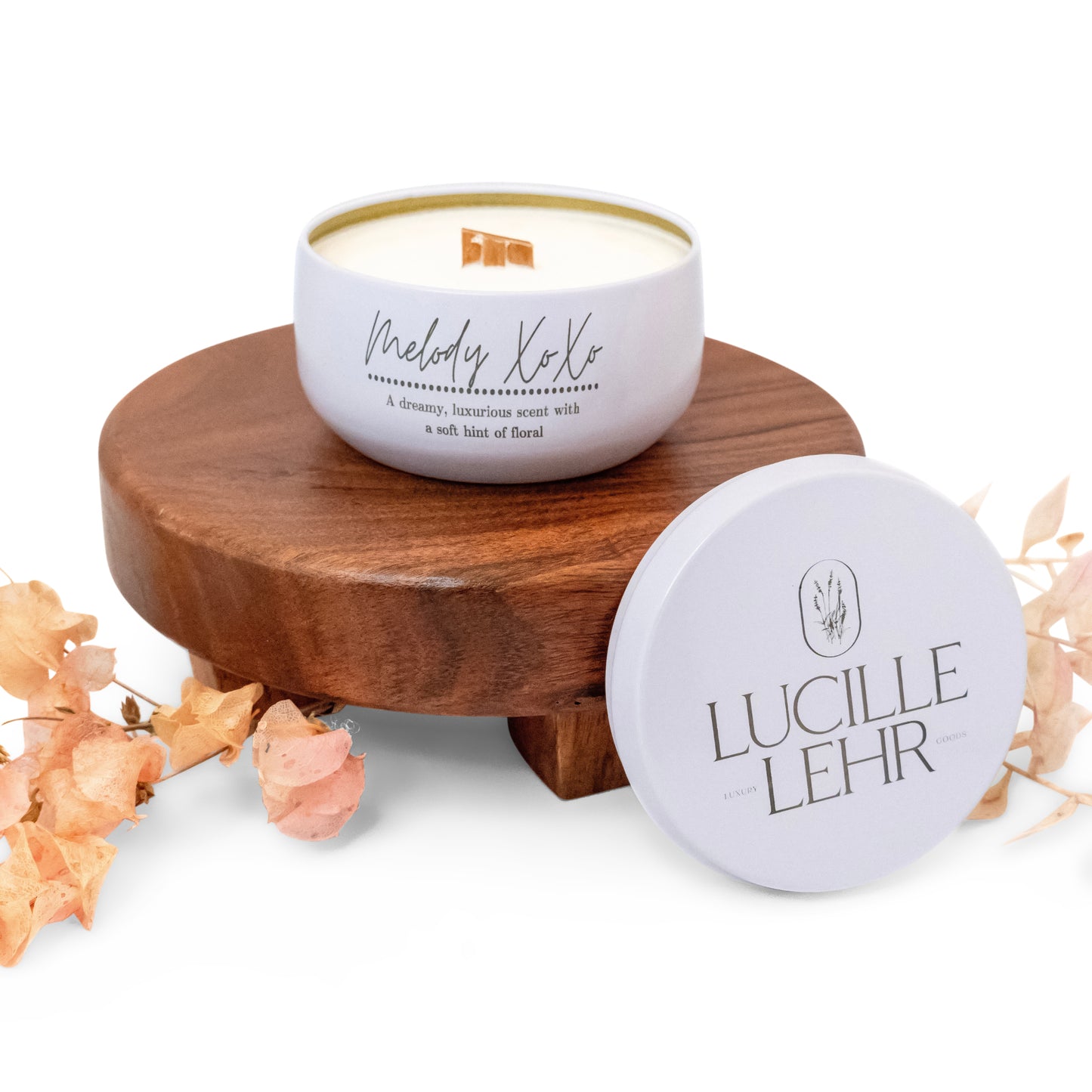 Lucille Lehr's 'Melody XoXo' Candle: Drift into a dreamy, luxurious ambiance with the 'Melody XoXo' candle, featuring a soft floral fragrance and a wooden wick for a cozy crackling sound. Packaged in an elegant white tin with a removable lid, this candle sits gracefully on a wooden stand, accented with delicate dried florals, making it a beautiful addition to any space.